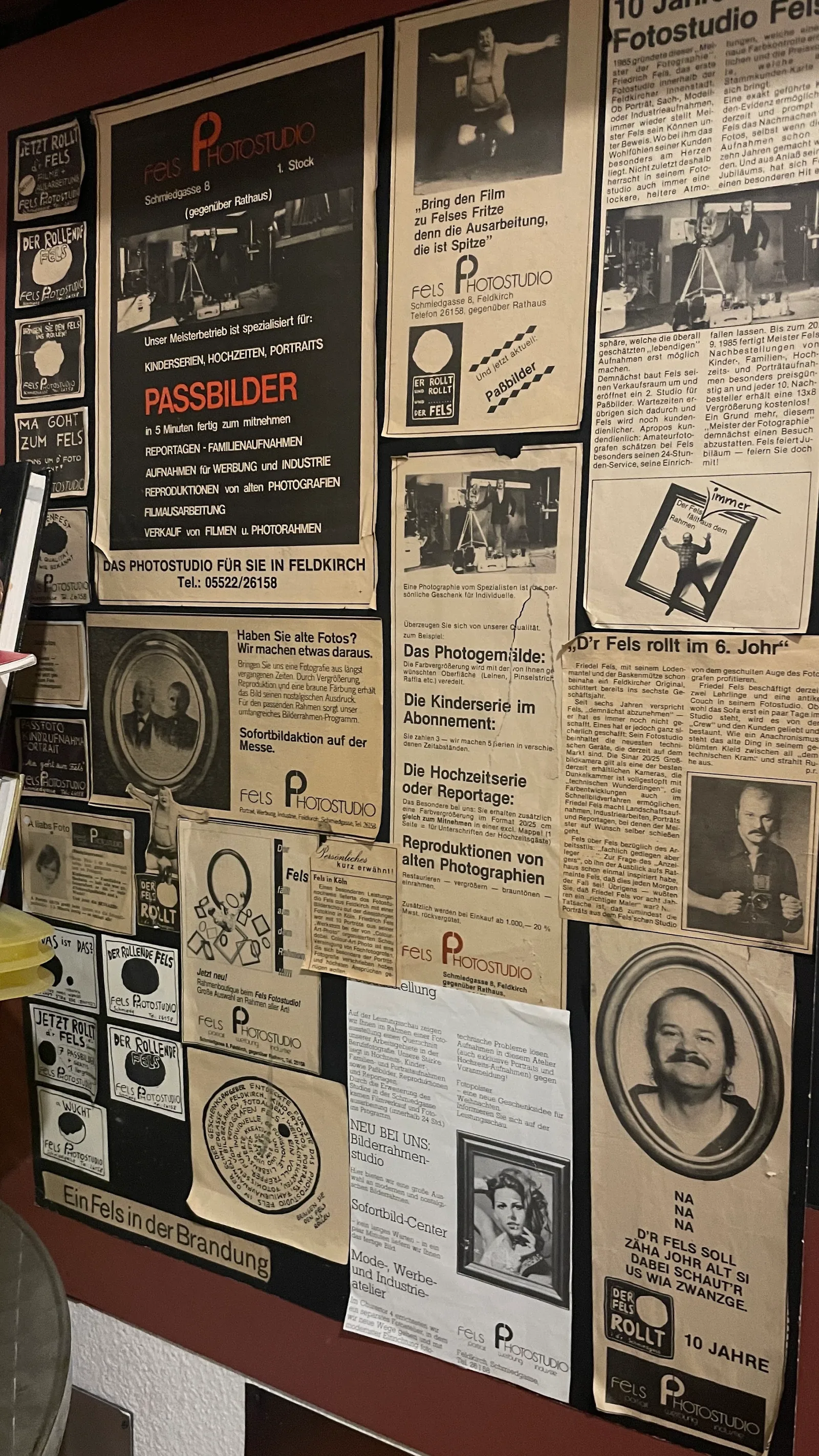 Wand im Studio, voll mit gerahmten Zeitungsanzeigen und Presseberichten des Betriebs aus den 1980er Jahren
